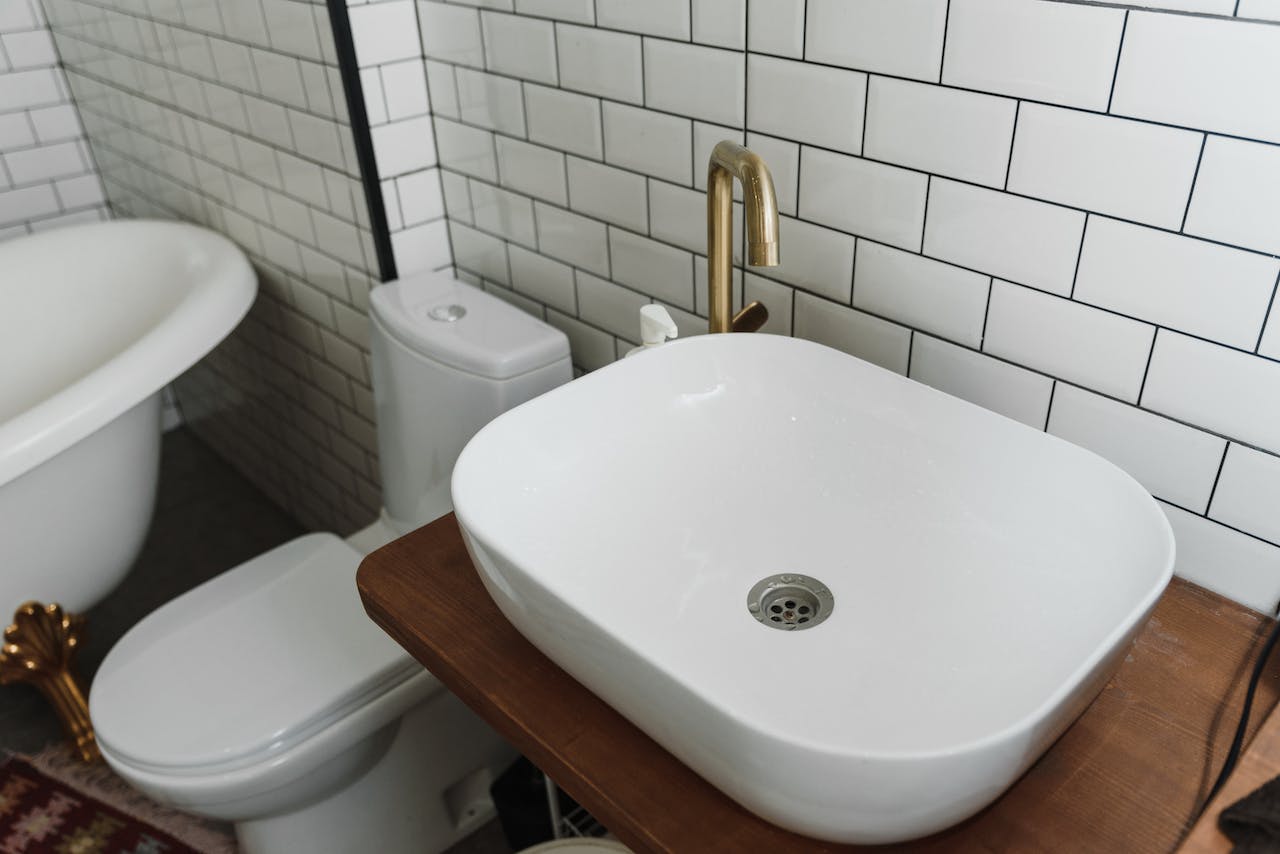 Na obrazku widać białą łazienkę z delikatnymi akcentami drewna, tworzącą przyjemną i harmonijną przestrzeń